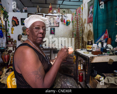 Une peau foncée mâle cubain qui est un croyant dans la regla de Ocha ou Santeria religion se trouve à l'intérieur de sa maison la peinture d'une poupée. Banque D'Images