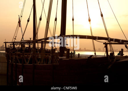 Silhouette d'un dhow au coucher du soleil au Koweït avec la ville en arrière-plan. Banque D'Images