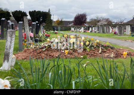 Des fleurs sur le haut d'un récemment creusé de sépulture dans cimetière Banque D'Images