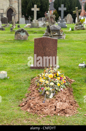 Des fleurs sur le haut d'un récemment creusé de sépulture dans cimetière Banque D'Images