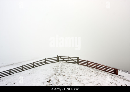 Une clôture en bois sur une digue de neige dans le brouillard. Banque D'Images