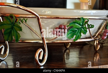 Plateau métal raisin lave détenteur d'un objet associé à la maison, assis sur une surface en bois. Le plateau est un plat de céramique blanche. Banque D'Images