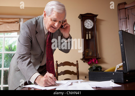 Un homme d'affaires sur un téléphone cellulaire et doing paperwork at home Banque D'Images