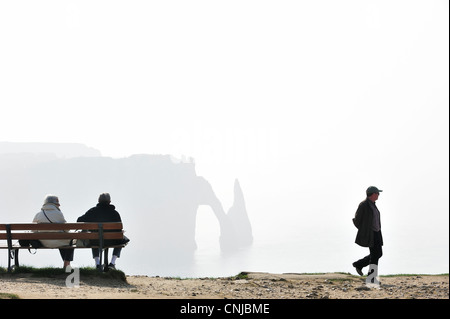 Personnes âgées touristes assis sur un banc en regardant la porte d'Aval, arche naturelle dans la falaise de craie à Etretat, Haute-Normandie, France Banque D'Images