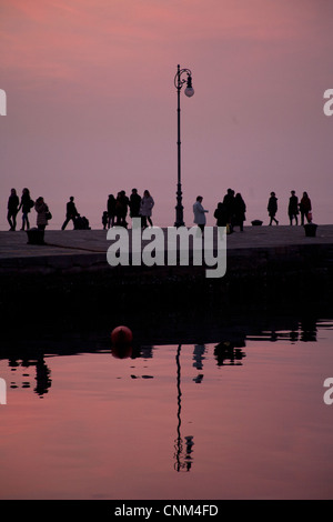 La réflexion des gens sur la jetée sur la mer au coucher du soleil, Trieste Italie Banque D'Images