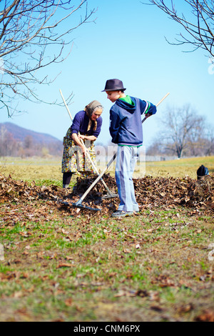 Grand-mère et petit-fils du grand ménage de printemps le verger de noyers avec râteaux Banque D'Images