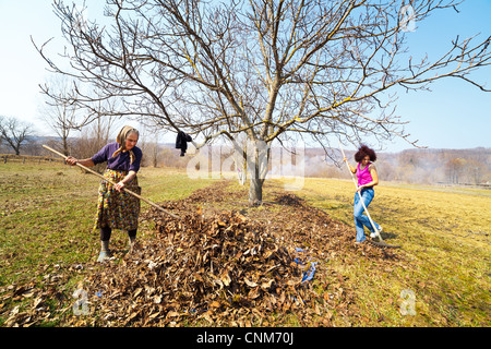 Hauts femme rurale et sa fille avec des râteaux, le nettoyage de printemps dans un verger de noyers Banque D'Images