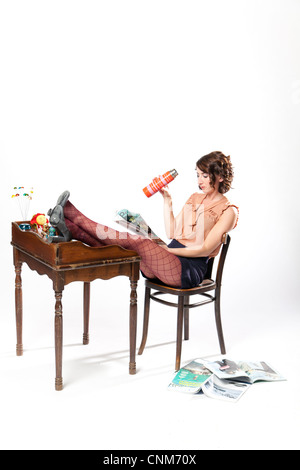 Une femme en vêtements rétro se détend avec ses pieds sur un vintage 24 la lecture d'un magazine et boire d'une thermos. Banque D'Images