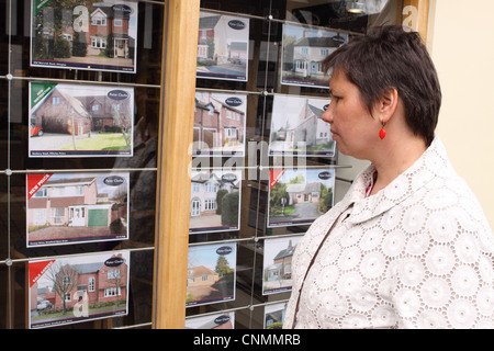 Femme à la propriété de maisons à vendre à une fenêtre d'agents immobiliers en Angleterre Banque D'Images