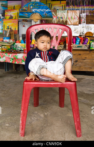 Portrait d'un vertical jeune Vietnamien à ennuyer assis dans une chaise en plastique rouge at a market stall. Banque D'Images