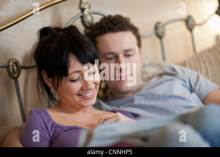 Couple reading newspaper in bed Banque D'Images