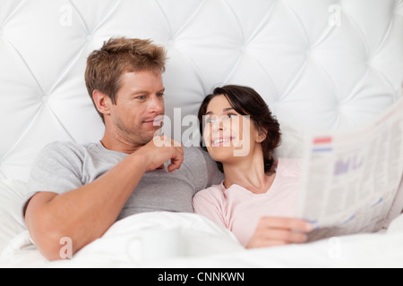 Smiling couple reading newspaper in bed Banque D'Images