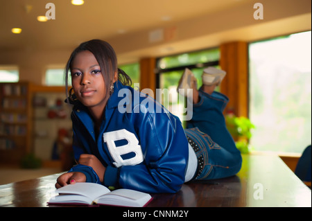 Young woman reading book couchée sur son ventre dans une bibliothèque Banque D'Images