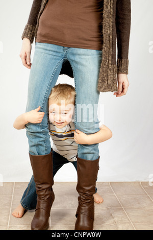Cute blonde boy dans un joyeux, ludique, attitude, avec les jambes de sa mère Banque D'Images