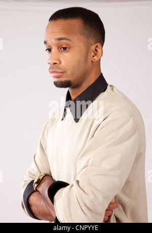 Beau jeune homme noir avec expression pensive et bras croisés, tourné vers la droite et vers le bas à la Banque D'Images