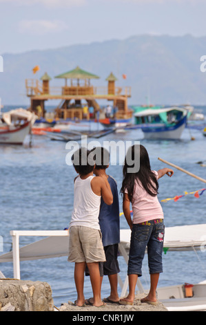 3 Les enfants d'Asie 2 garçons 1 fille pointant à la recherche de navires à quai, à Sabang, Puerto Galera, Philippines, en Asie du sud-est Banque D'Images