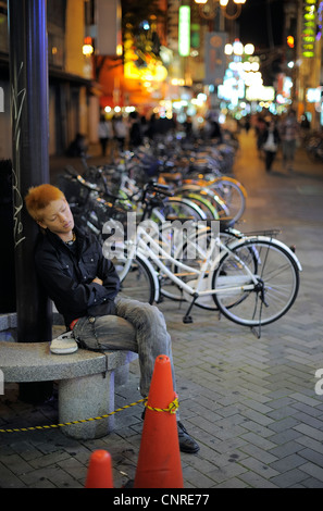 Jeune homme japonais dormir assis sur le banc en pierre, Osaka, Japon Banque D'Images