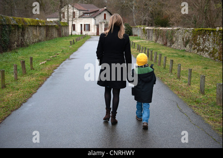 La mère et le fils marche sur chemin dans village, tenant les mains, vue arrière Banque D'Images