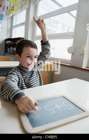 Garçon assis au bureau avec tableau, main levée Banque D'Images