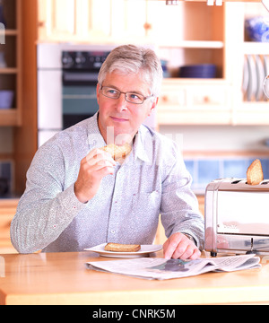 Middle aged man eating toast pour le petit déjeuner dans la cuisine. Banque D'Images