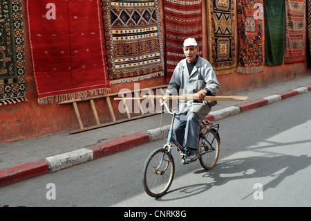 Un menuisier porte quelques bois sur sa bicyclette passé le souk aux tapis, Marrakech Maroc Banque D'Images