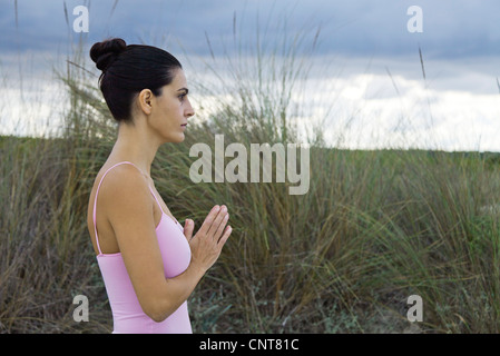 Femme mature en position de prière en plein air, side view