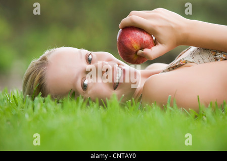 Young woman lying on grass holding apple Banque D'Images