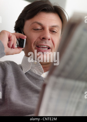 Middle aged man reading stock listings et la négociation sur le téléphone de la maison Banque D'Images