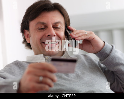Portrait of happy young middle aged man sitting on sofa, conversation au téléphone sans fil et l'achat par carte de crédit Banque D'Images
