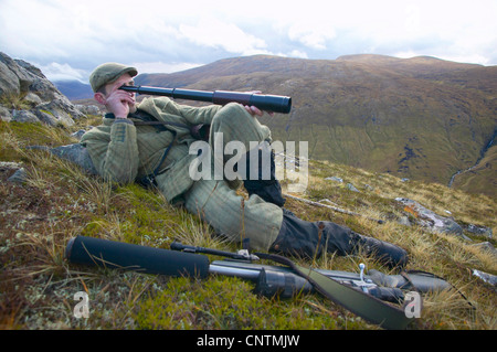 Stalker allongé dans l'herbe sur un versant de montagne à la recherche vers le bas dans la vallée d'une rivière à travers un télescope, Royaume-Uni, Ecosse, Sutherland, Alladale Wilderness Réserver Banque D'Images