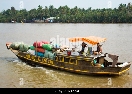 Vue horizontale d'un petit bateau motorisé en bois portant un arc plein de marchandises le long du Delta du Mékong, Vietnam Banque D'Images