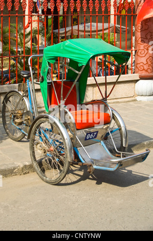 Vue verticale d'un cycle-rickshaw vide cyclo ou en stationnement sur la chaussée dans l'ancienne ville de Hoi An, Vietnam sur une journée ensoleillée. Banque D'Images