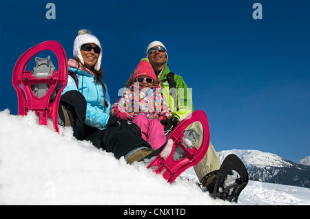 Famille de trois assis dans la neige à une pente au cours de la raquette sur les vacances à la montagne, France Banque D'Images