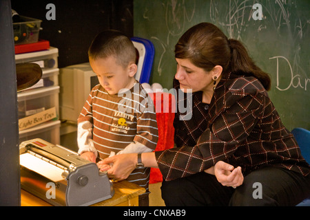 Avec l'aide d'un membre du personnel formé un garçon aveugle sur une machine à écrire braille types à l'intention des enfants aveugles Centre d'apprentissage. Banque D'Images