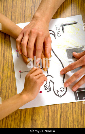 Un des guides de l'enseignant un enfant aveugle, les mains sur les grandes lignes d'un lézard dans soulevées dans un type de classe d'écriture des besoins spéciaux. Banque D'Images