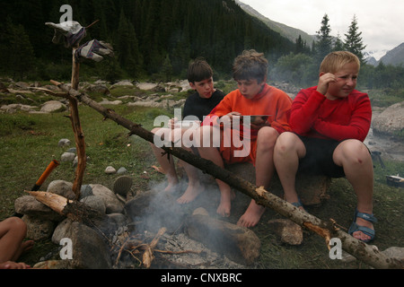 Les enfants mangent à côté d'un feu de camp dans la vallée de Terskey Ala-Too Randonnées Jeti-Oguz de montagnes de Tian Shan, au Kirghizistan. Banque D'Images