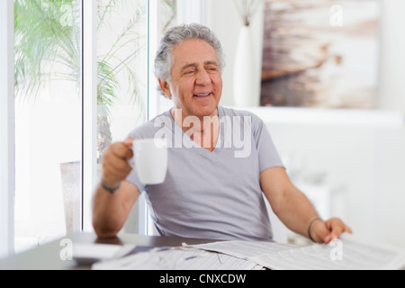 A cheerful senior homme tenant une tasse de café et un journal Banque D'Images