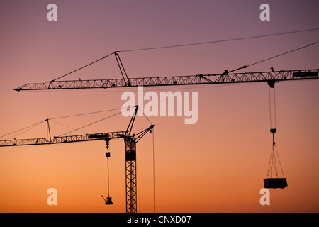 Deux grues de construction silhouetted against a sunset sky Banque D'Images