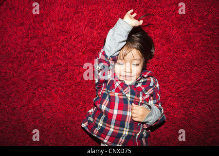 Un jeune garçon souriant allongé sur un tapis rouge Banque D'Images