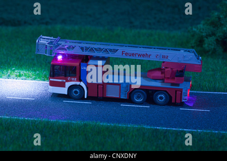 Un diorama d'un camion de pompiers jouet miniature roulant sur une route de nuit Banque D'Images