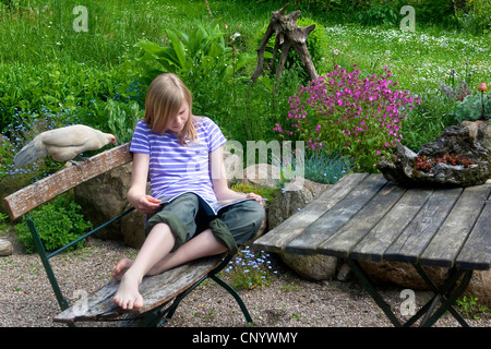 Bantam (Gallus gallus f. domestica), une jeune fille assise dans un jardin avec un curieux et cultivé et chick lit un magazine, Allemagne Banque D'Images