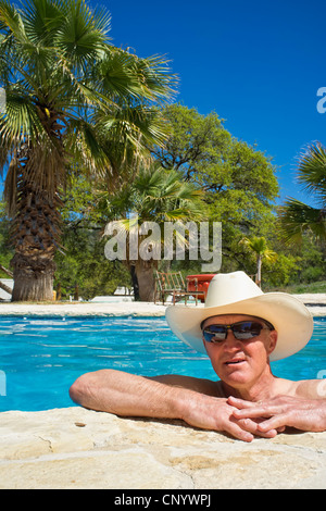 Homme d'âge moyen avec des lunettes de soleil et chapeau de cow-boy et rafraîchissant dans une piscine de détente Banque D'Images