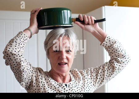 Middle aged woman holding casserole au-dessus de sa tête à la perplexe Banque D'Images