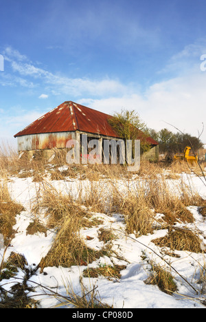 Vieux bâtiment de ferme utilisée pour stocker des machines agricoles dans l'hiver avec neige au sol Banque D'Images