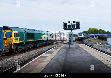 Une locomotive Classe 66 Freightliner à la tête d'un train de wagons de transport de conteneurs, tandis qu'un train part de passager sur une autre ligne. Banque D'Images