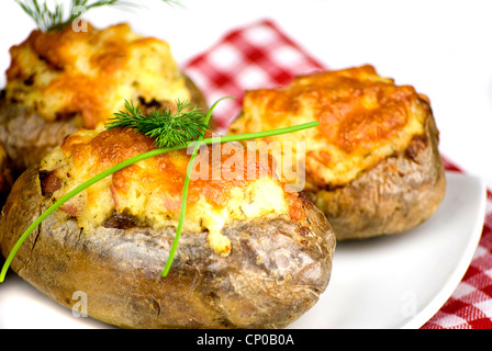 Pommes de terre farcies de fromage cheddar couverte décorée de ciboulette et de feuilles d'aneth dans une assiette blanche Banque D'Images