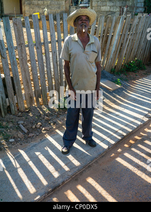 De 60 à 70 ans se situe à l'avant les hommes hispaniques et fume un cigare tôt le matin par une clôture d ombre à Viñales, Cuba. Banque D'Images