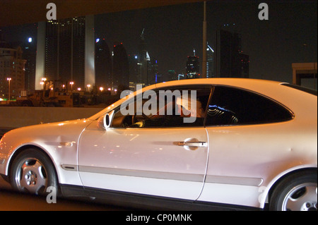 Un homme en costume traditionnel arabe au volant d'une Mercedes, la nuit à Dubaï, Émirats Arabes Unis Banque D'Images