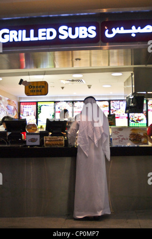 Homme dans la robe arabe traditionnelle au comptoir du restaurant Charleys Grilled Subs aéroport international de Dubaï, Dubaï, Émirats arabes Unis Banque D'Images