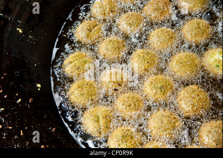Boules de mélange de pois chiches assaisonnées sont frits dans l'huile pour faire des falafels dans un décrochage à rue dans la ville cisjordanienne de Bethléem. Banque D'Images